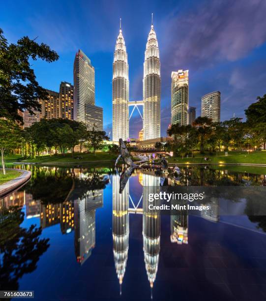 illuminated petronas towers building in kuala lumpur, malaysia at dusk. reflection in lake. - kuala lumpur photos et images de collection