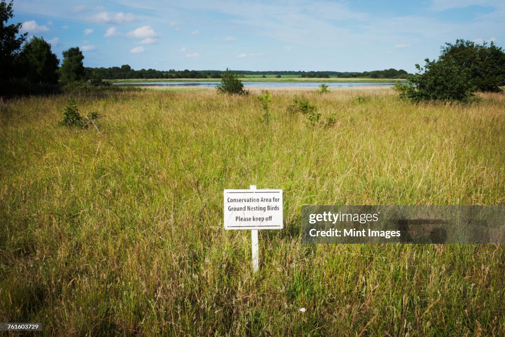 White Keep Off sign on a meadow with river and trees in the distance.