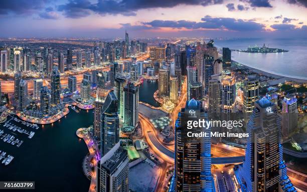 aerial view of the cityscape of dubai, united arab emirates at dusk, with illuminated skyscrapers and the marina in the foreground. - middle east stock pictures, royalty-free photos & images