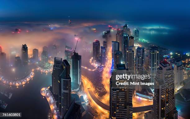 aerial view of the cityscape of dubai, united arab emirates at dusk, with illuminated skyscrapers and the marina in the foreground. - destination fashion 2016 stock pictures, royalty-free photos & images