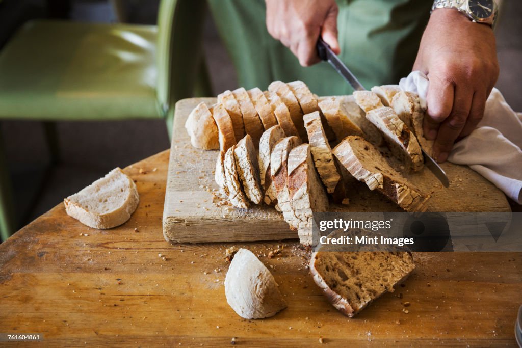 Close up high angle view of person slicing freshly baked loaf of bread.