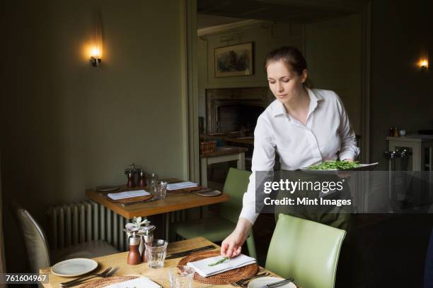 woman wearing apron setting table in a restaurant. - waitress foto e immagini stock