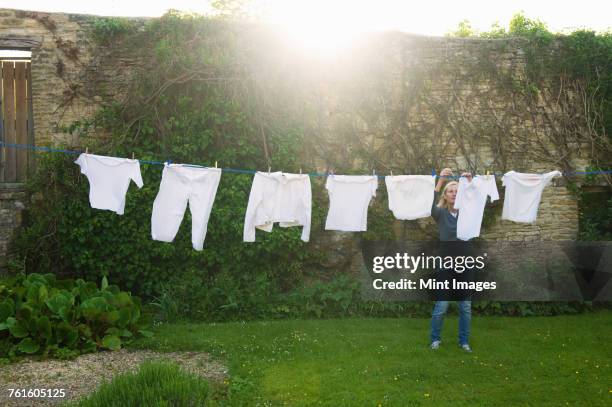 woman standing on a lawn in a garden, hanging up laundry on washing line. - clothesline stock pictures, royalty-free photos & images