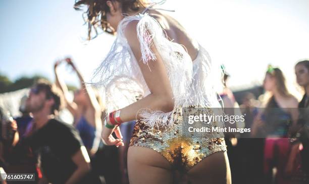 young woman at a summer music festival wearing golden sequinned hot pants, dancing among the crowd. - sequin shorts stock pictures, royalty-free photos & images