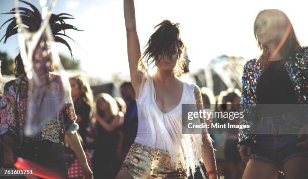 young woman at a summer music festival wearing golden sequinned hot pants, dancing among the crowd. - festivalganger stockfoto's en -beelden