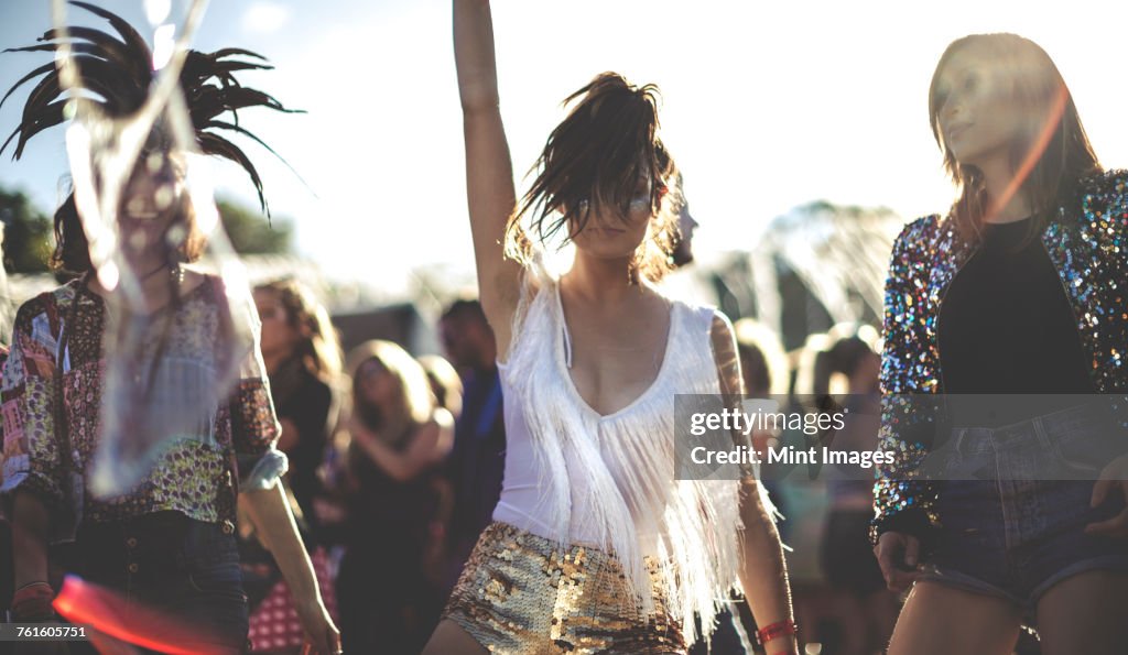 Young woman at a summer music festival wearing golden sequinned hot pants, dancing among the crowd.