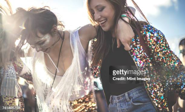 two young women at a summer music festival wearing sequins with painted faces laughing and dancing. - music festival 2016 weekend 2 stock-fotos und bilder