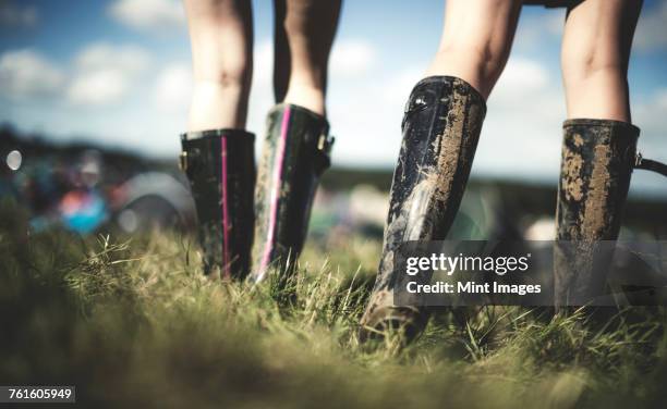 low section rear view of two young women at a summer music festival wearing muddy wellington boots. - rubberlaars stockfoto's en -beelden