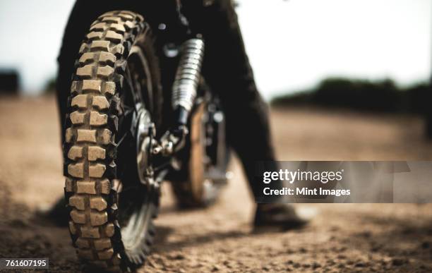 rear view of man sitting on cafe racer motorcycle on a dusty dirt road, close up of tire. - dirt road motorbike stock pictures, royalty-free photos & images