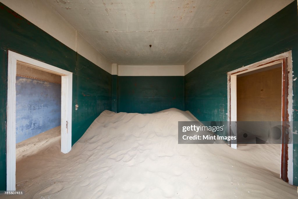 A deserted building, a room with painted walls and two doorways, and a heap of sand engulfing half the room. 