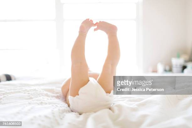 baby girl (6-11 months) lying down on bed with feet in air - barefoot feet up lying down girl stockfoto's en -beelden