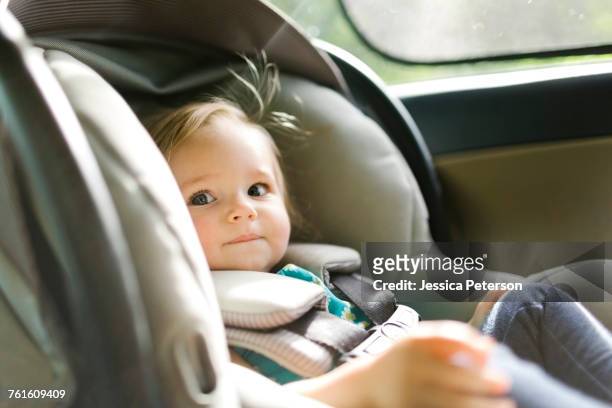 baby girl (12-17 months) sitting in baby car seat during car trip - child car seat foto e immagini stock