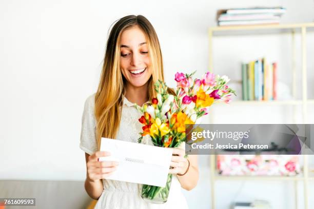 beautiful woman reading letter and holding flowers - woman flowers stockfoto's en -beelden