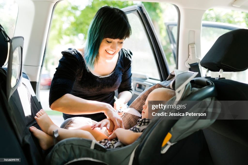 Mother fastening baby boy (12-17 months) in car seat