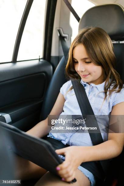 girl ( 8-9) sitting in car and using digital tablet - midway foto e immagini stock