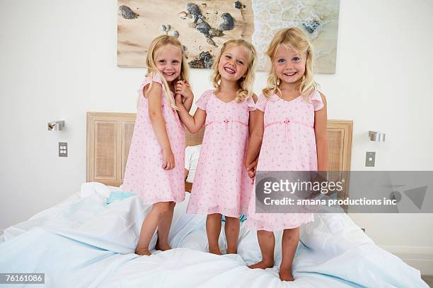 triplets standing on bed (portrait) - triplet girls stock pictures, royalty-free photos & images
