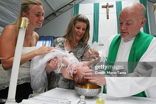 Priest Cuthbert O'Connell baptizes baby Trish Cucurullo as mother Sheena Cucurullo and godmother Shannon Ball assist following Sunday Mass at Saint...