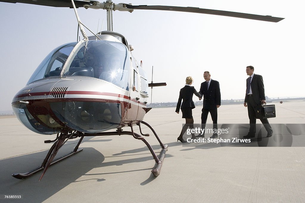 Businesswoman greeting two businessman by a helicopter