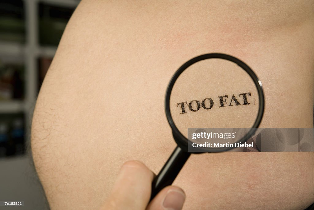 A person holding a magnifying glass to a man's abdomen stamped 'Too Fat'