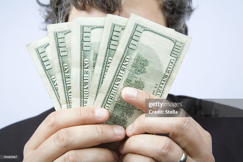 A businessman holding a fan of hundred dollar bills in front of his face