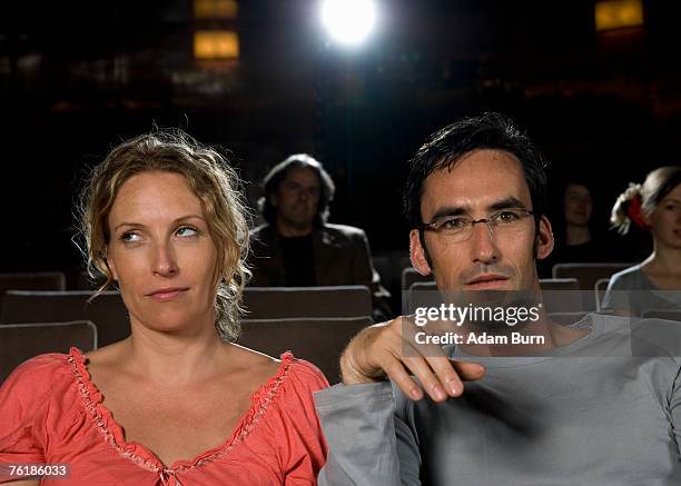 a woman rolling her eyes whilst sitting next to a man in a movie theater - unangenehmes rendezvous stock-fotos und bilder