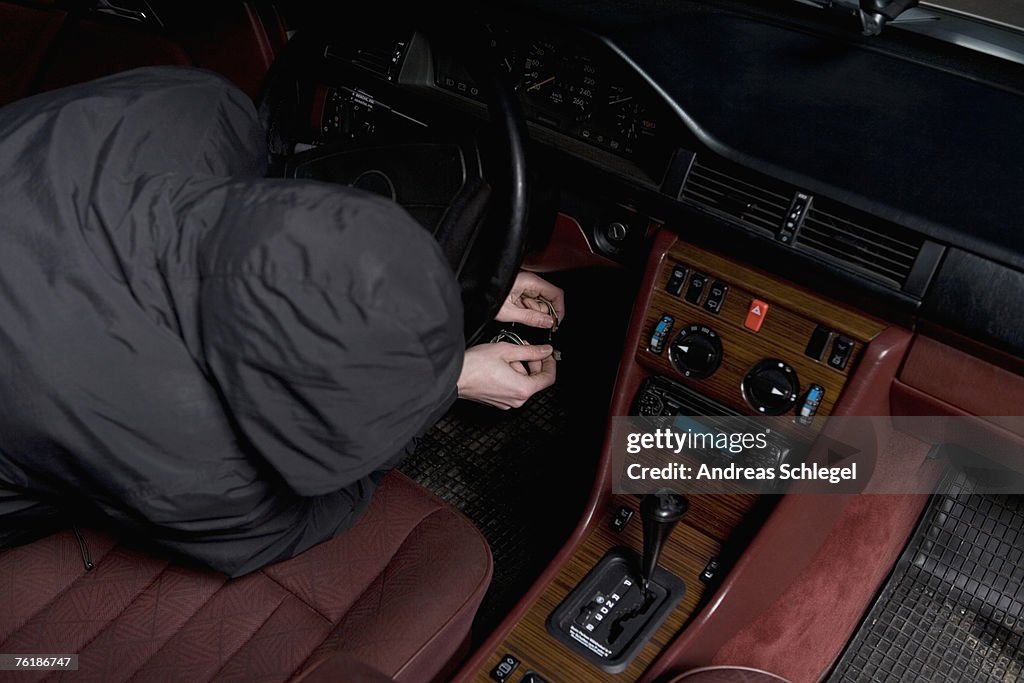 A hooded man starting a car with ignition circuit wires