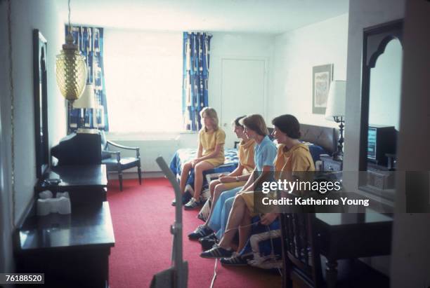 Group of four uniformed chambermaids sit on the beds in a room at an unidentified hotel and watch television, July 1978.