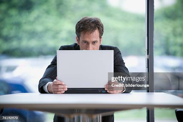 portrait of businessman hiding behind laptop computer - hiding behind laptop stock pictures, royalty-free photos & images
