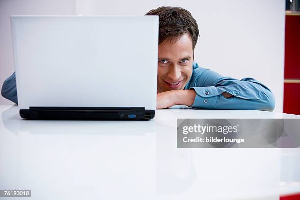 portrait of businessman peeking behind laptop computer - hiding behind laptop stock pictures, royalty-free photos & images