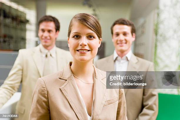 portrait of young businesswoman with two male colleagues in the background - portrait man suit smiling light background stock pictures, royalty-free photos & images
