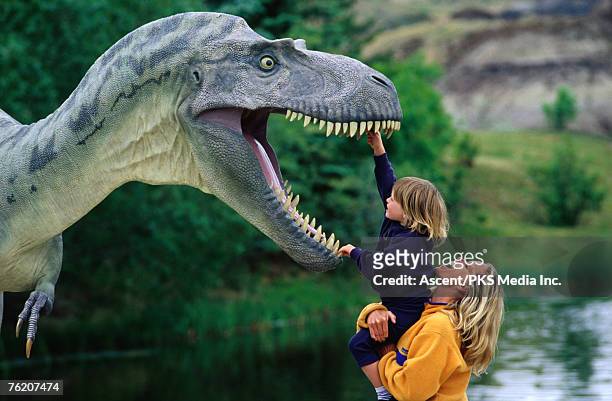 woman holding a girl up to a dinosaur model, drumheller valley, alberta, canada, north america - drumheller stock pictures, royalty-free photos & images