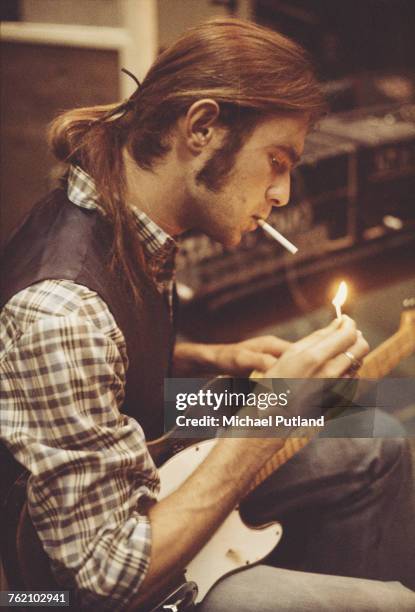 English musician, singer and guitarist with rock group Status Quo, Francis Rossi pictured ligting a cigarette with a green Fender Telecaster guitar...