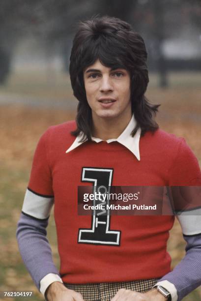 Australian singer-songwriter Rick Springfield pictured wearing a red and purple knitted jumper in a park in London in 1973.