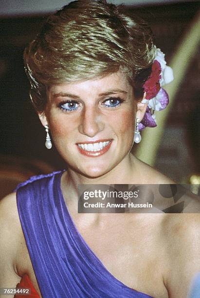 Diana, Princess of Wales, wearing a red and purple chiffon evening dress designed by Catherine Walker with silk flowers in her hair, attends a dinner...