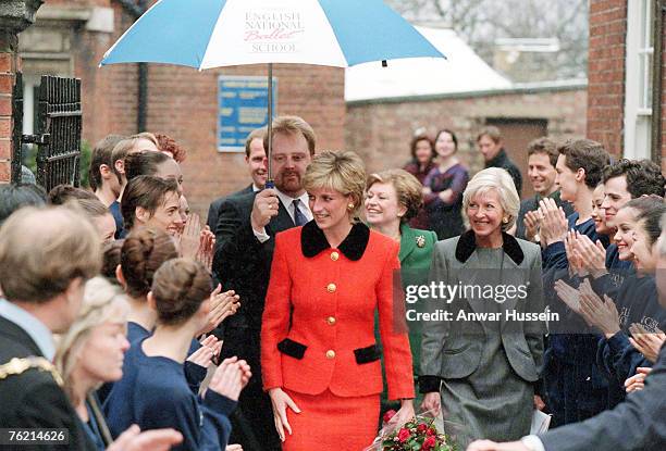 Diana, Princess of Wales, wearing a red suit with a black collar and gold button, shelters under an umbrella as she visits the English National...