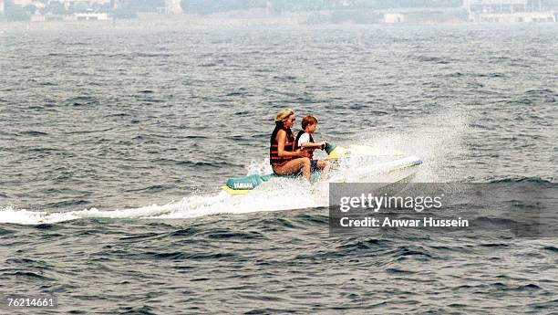 Diana, Princess of Wales, wearing a life jacket over her swimsuit and sunglasses, rides on a jet ski with Prince Harry on July 17, 1997 in...