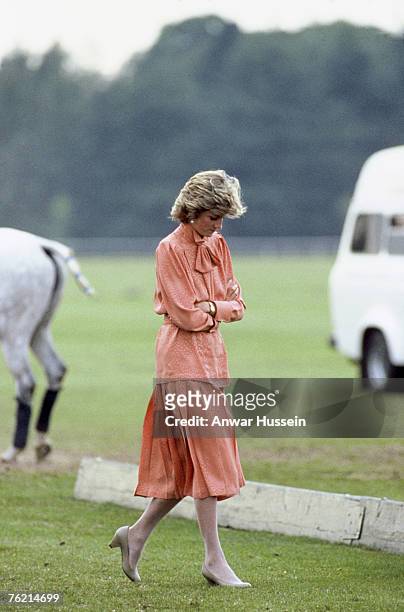 Diana, Princess of Wales, wearing a peach dress with a pussy bow tie and pleated skirt designed by Jan Van Velden, attends a polo match at Guards...