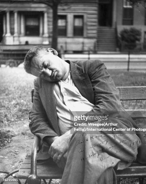 Polish-born American photographer Arthur 'Weegee' Fellig sleeps on a park bench, 1940s. The picture is signed in the lower right corner and reads 'To...