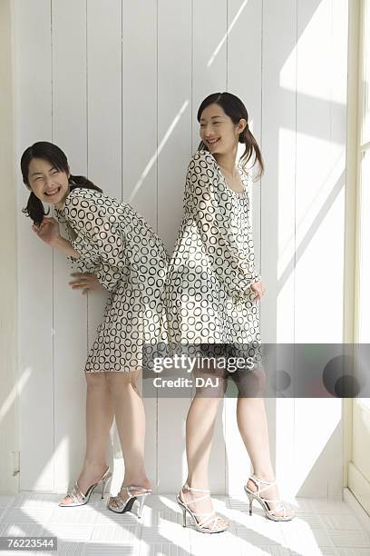 twin sisters standing back to back, smiling, side view - leaning over stock pictures, royalty-free photos & images