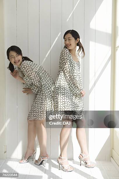 twin sisters standing back to back, smiling, side view - woman bending over imagens e fotografias de stock