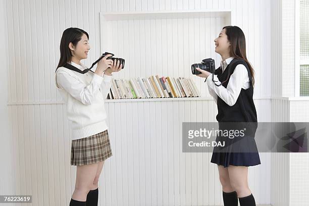 twin sisters smiling and holding cameras, side view - 若い カワイイ 女の子 日本人 ストックフォトと画像