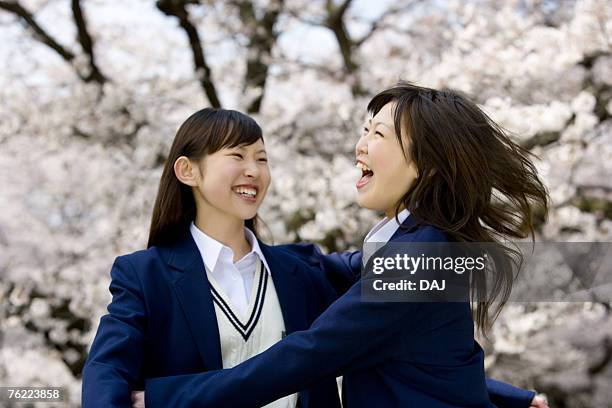 teenage girls jumping and smiling under cherry trees, front view, side view, japan - estudiante de bachillerato chica fotografías e imágenes de stock