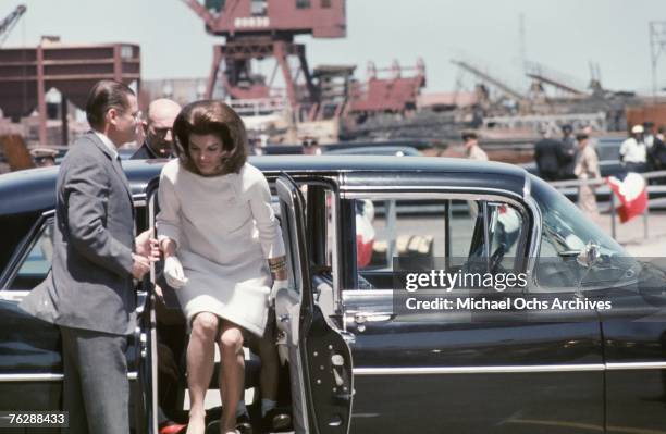 Secretary of Defense Robert McNamara helps former First Lady Jacqueline Kennedy out of her car before a ceremony to christen the USS John F. Kennedy...