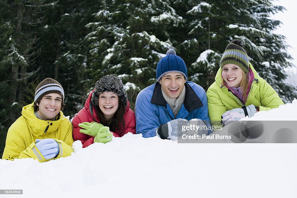 Two young couples lying in snow near forest, portrait