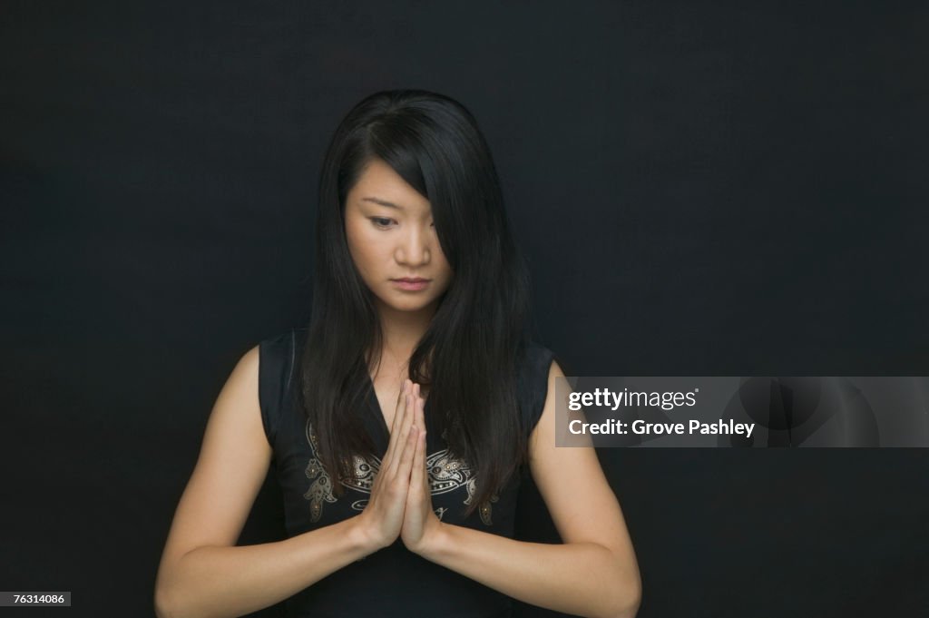 Young woman against black background, holding hands in prayer position