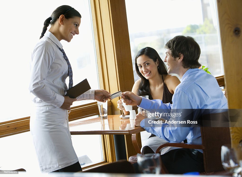Waitress accepting credit card from young couple in restaurant