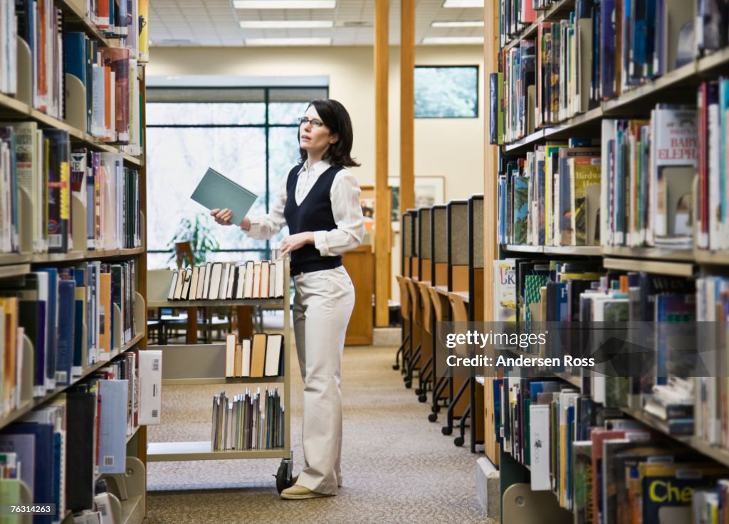 Female librarian returning books to shelves in library