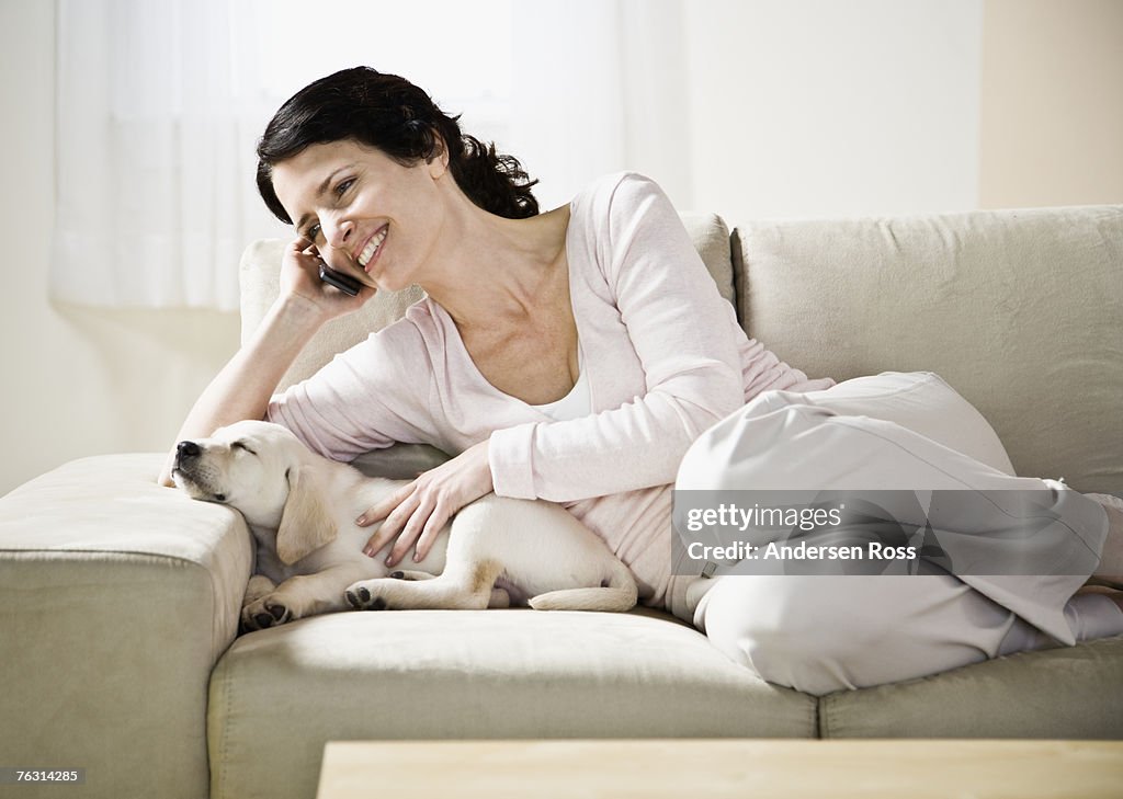 Mid adult woman sitting on sofa with puppy dog asleep