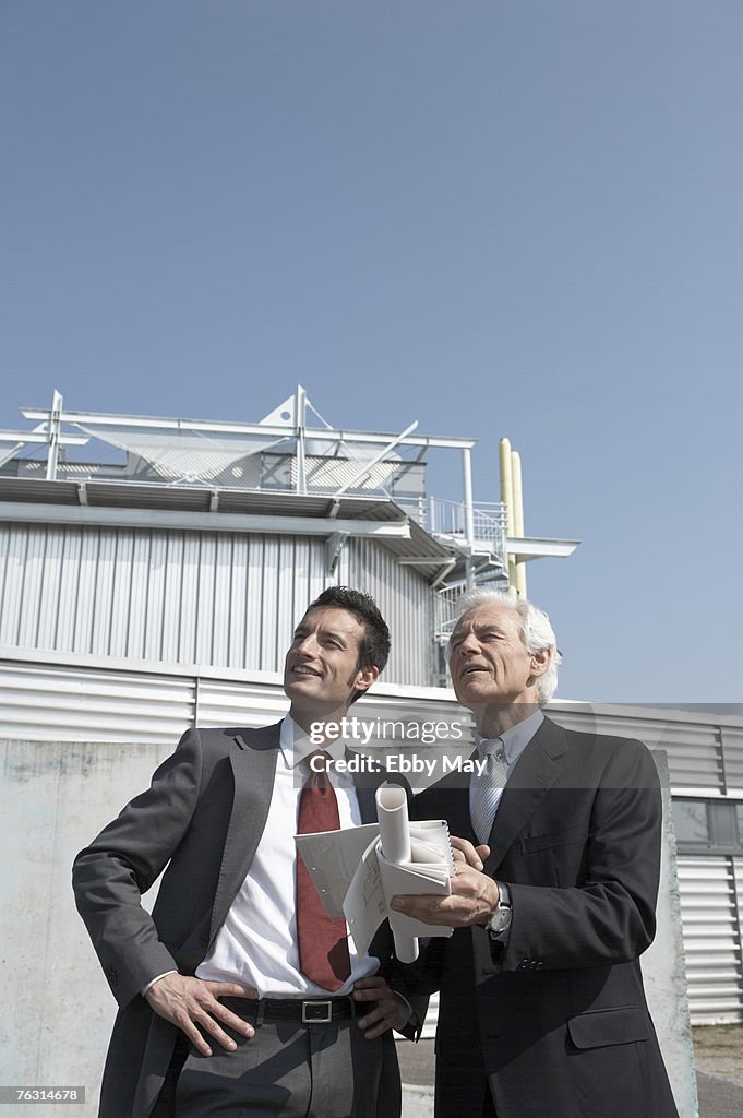 Two men standing outside building with plan, low angle view