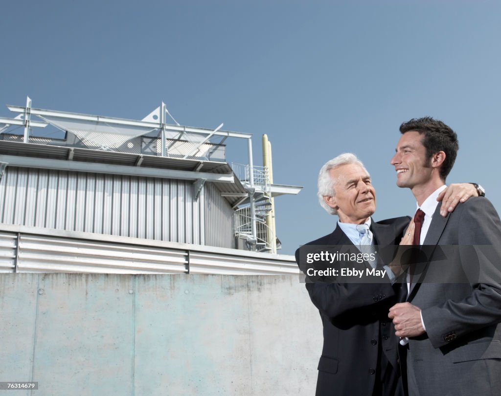 Senior man putting arm around man in front of industrial building
